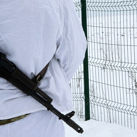 An armed border guard stands before a fence at the Ukraine-Russia border, Kharkiv Region, northeastern Ukraine, February 16, 2022.